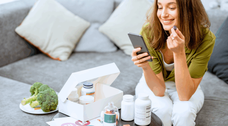 Smiling woman taking supplements while reading on smartphone, surrounded by vitamins and healthy food – illustrating biohacking for enhanced skin treatments on Look Lovely London blog