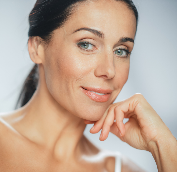 Confident woman with radiant, natural-looking skin, smiling softly in a bright, elegant clinic setting—reflecting the subtle, rejuvenating results of advanced aesthetic treatments offered by Dr Davina in Bishop’s Stortford